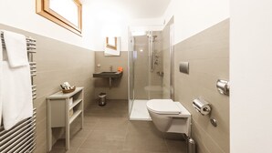 Een moderne badkamer met een douche met glazen wand, een toilet, een wastafel en een handdoekrek.