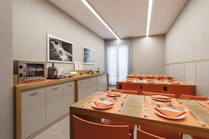 Un comedor moderno con sillas y mesas anaranjadas, equipado con vajilla básica y una máquina de café.