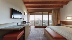Une chambre d’hôtel compacte dotée d’une kitchenette, d’un lit avec un banc rouge, d’un téléviseur fixé au mur et d’un balcon avec vue.