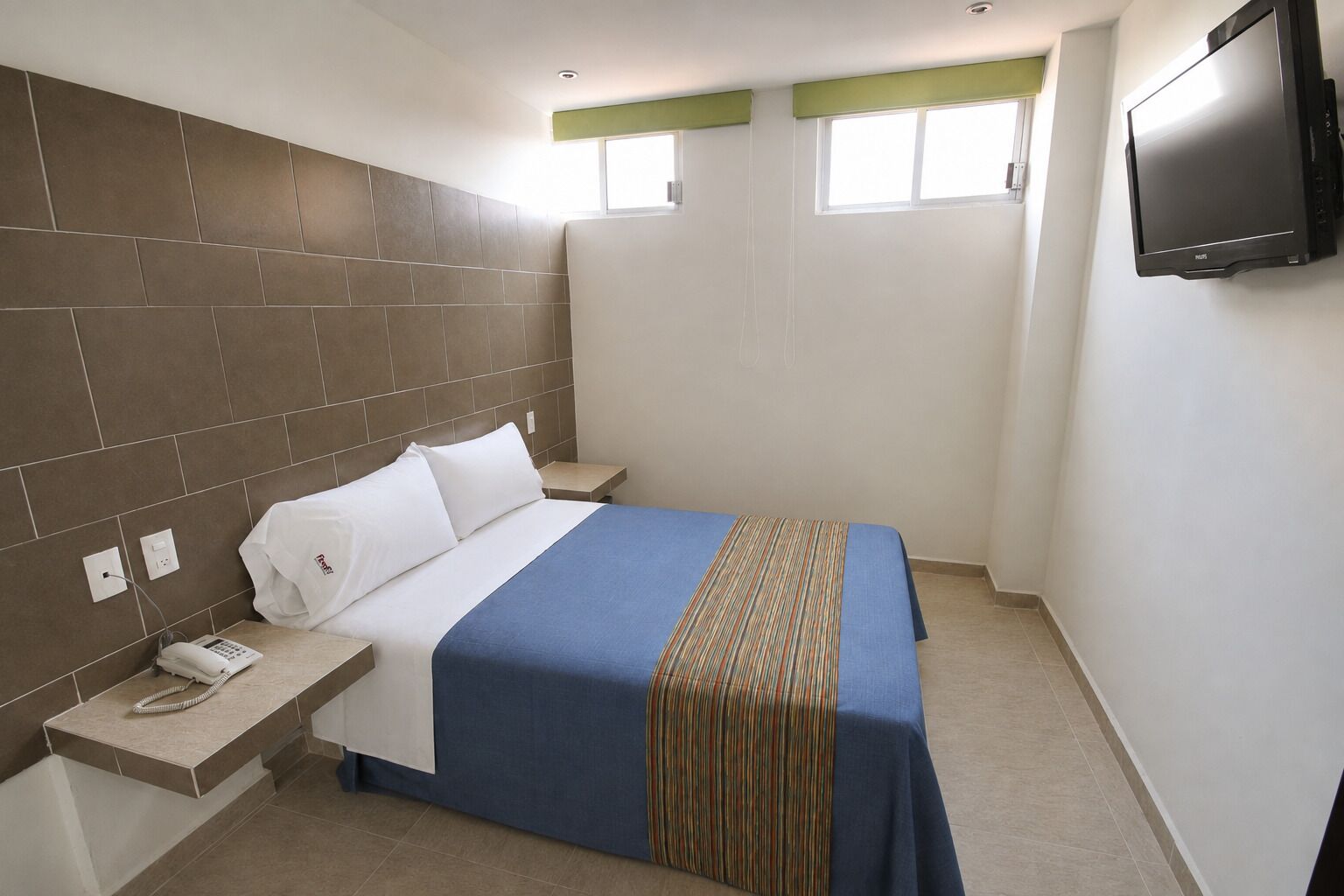 A hotel room with a bed, a bedside table with a phone, a TV mounted on the wall, and a window with a view.