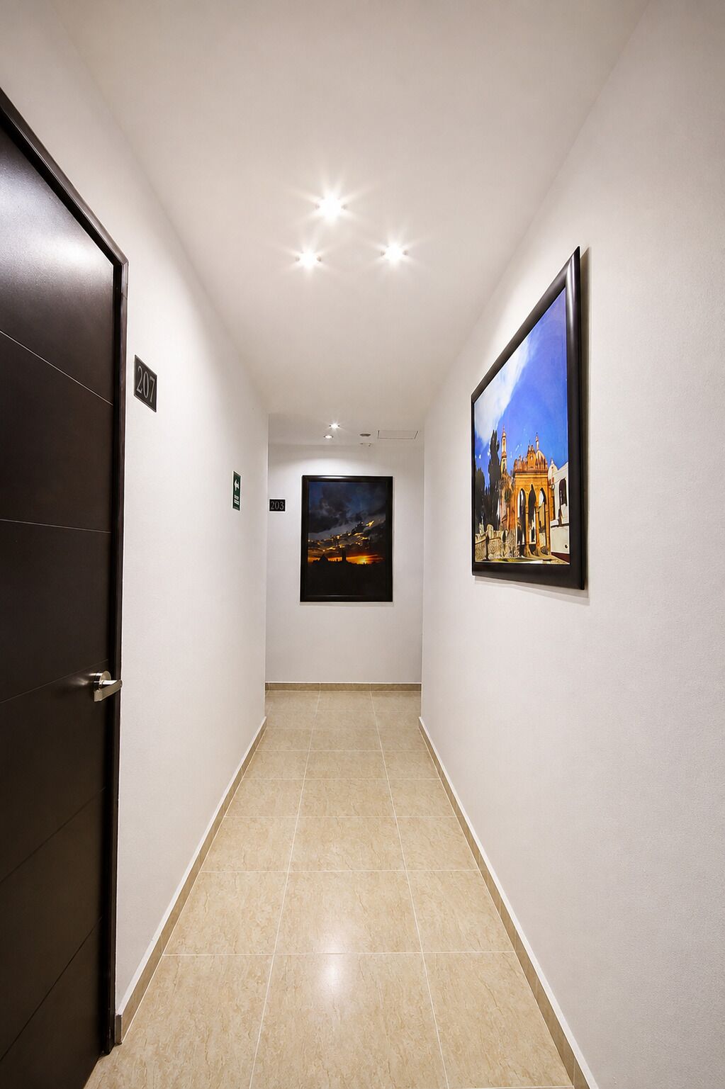 A hallway with a door labeled '207', a framed picture on the wall, and a tiled floor.
