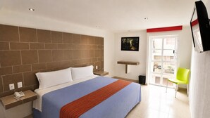 A hotel room with a large bed, a bedside telephone, a small table, a chair, a window, and a door.