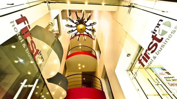 A hotel interior with a central spiral staircase, multiple balconies, and a chandelier. - First Inn Hotel & Business (Texcoco de Mora)