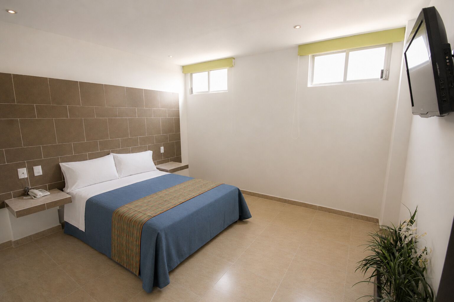Quarto de hotel com cama, mesa de cabeceira e televisão fixada na parede.