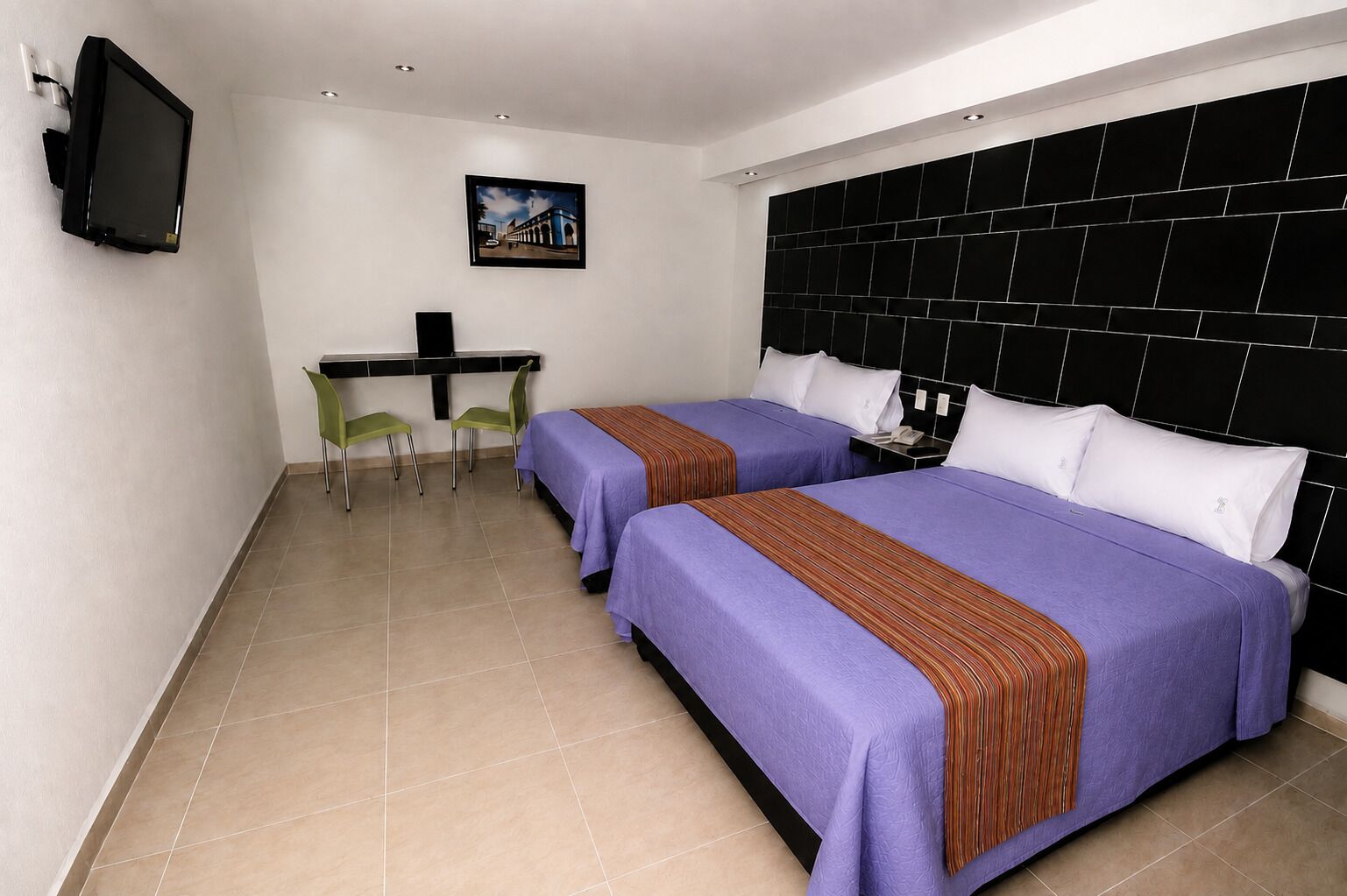 A hotel room with two beds, a desk, chairs, and a television.