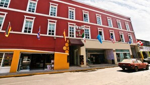 A red building with multiple flags, a hotel sign, and a parked car.