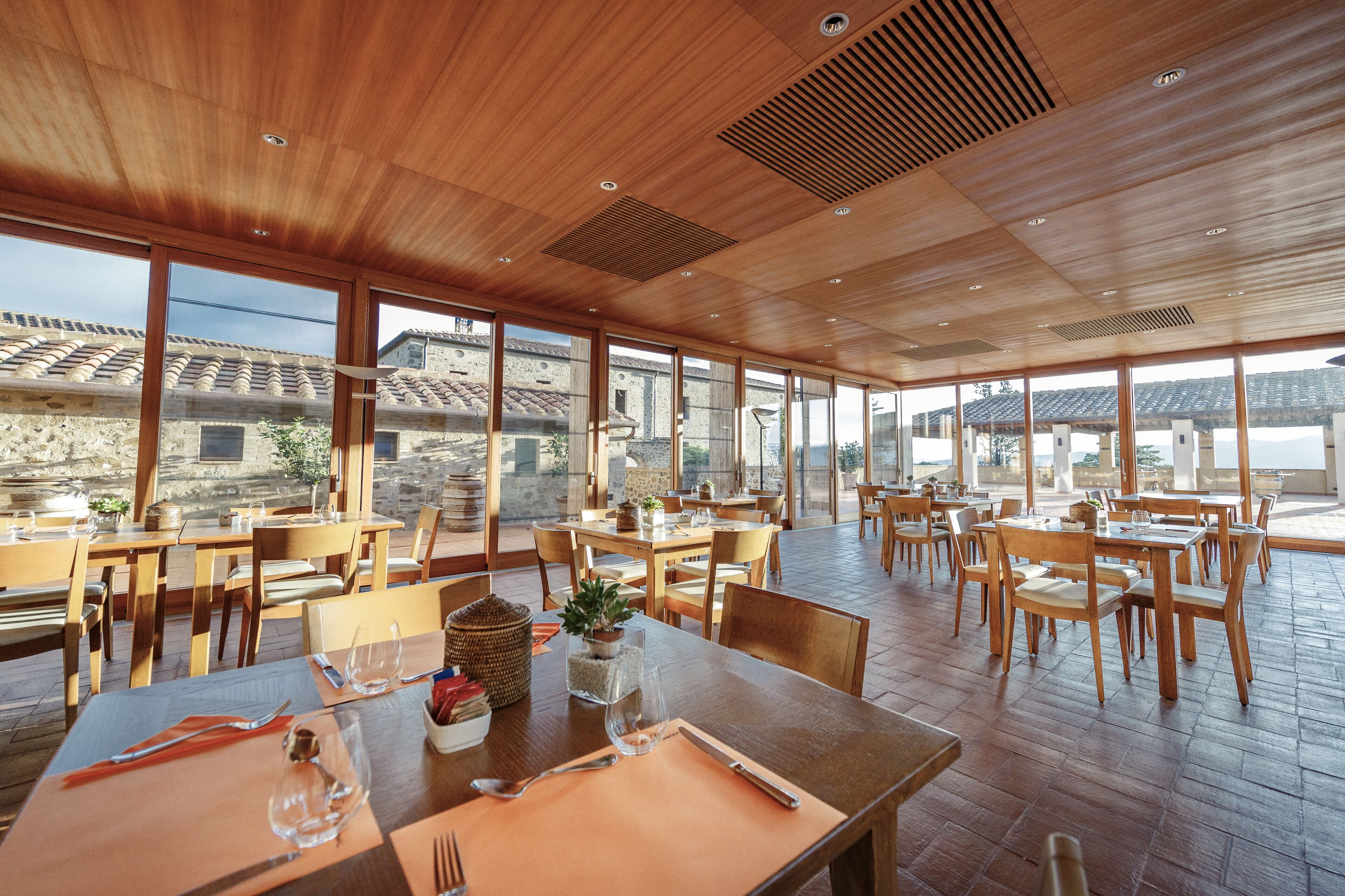Ein geräumiges Restaurant mit Holztischen und -stühlen, große Fenster mit Blick auf die umliegende Architektur.
