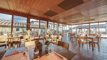 Ein geräumiges Restaurant mit Holztischen und -stühlen, große Fenster mit Blick auf die umliegende Architektur.