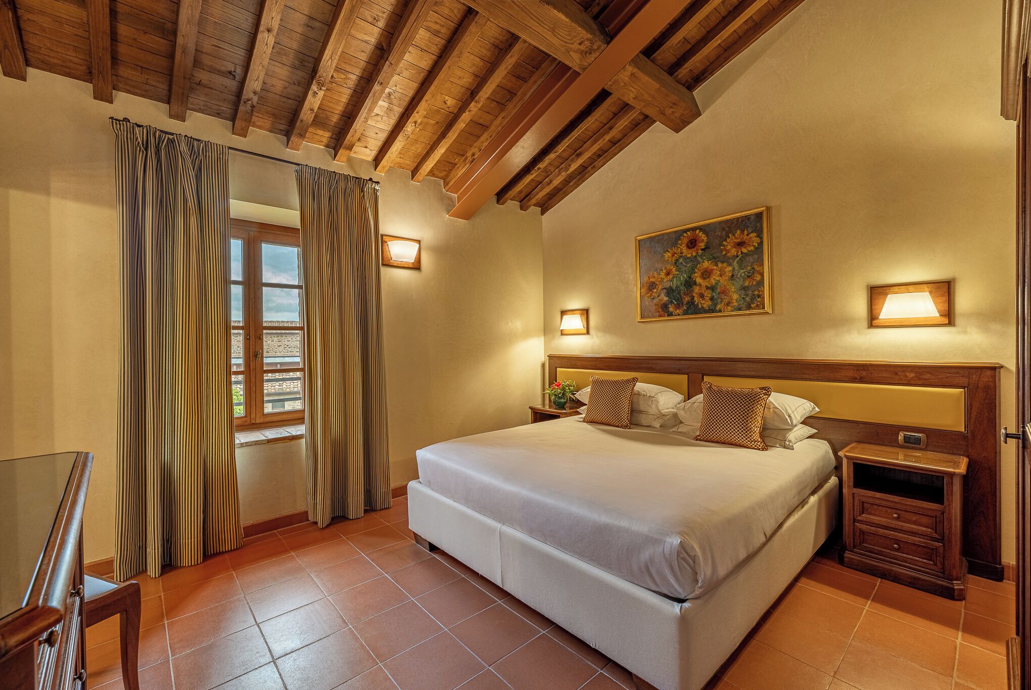 Un dormitorio con una cama grande, cabecera de madera, dos mesitas de noche y una ventana con cortinas.