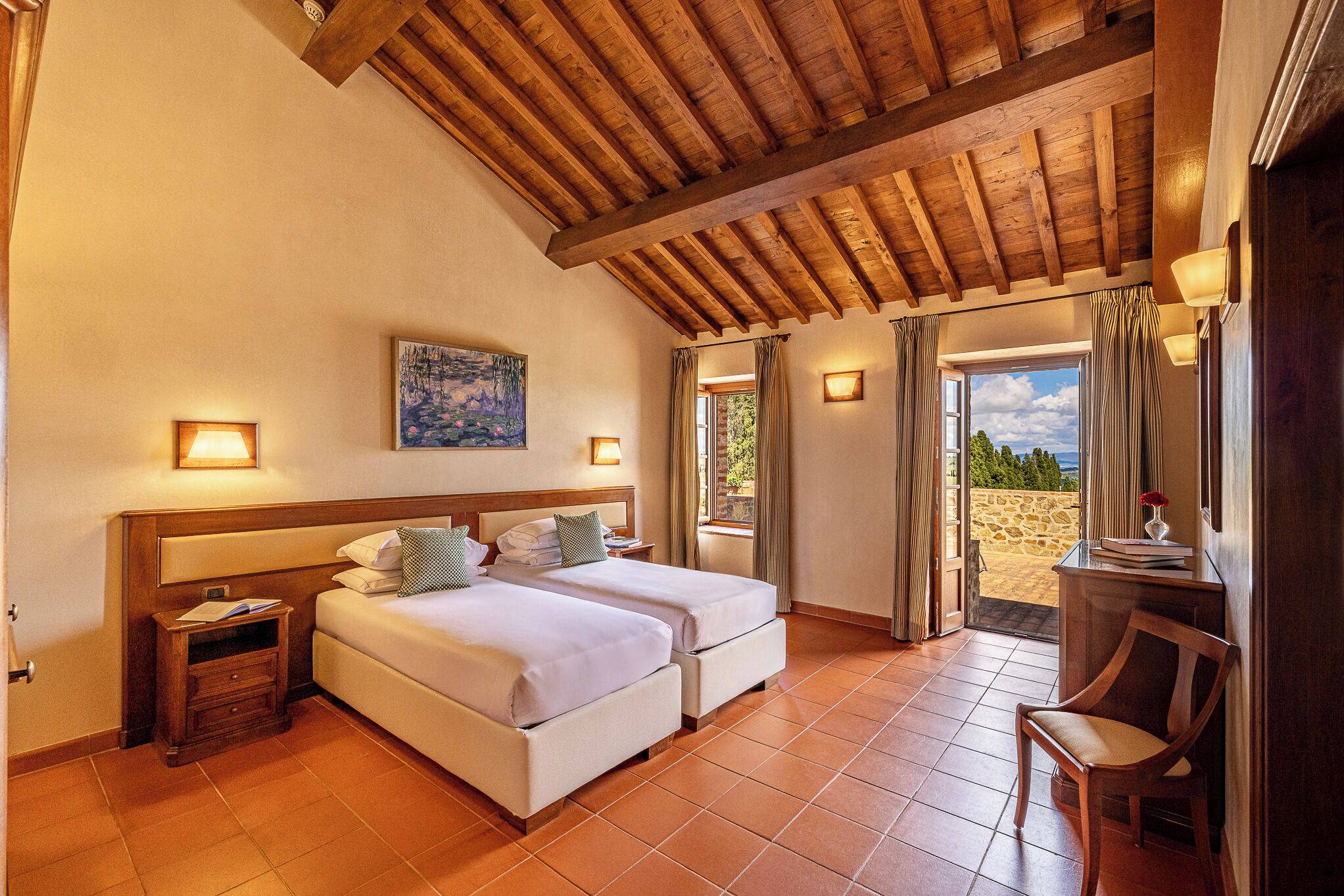 A bedroom with two beds, a wooden ceiling, a painting, and a view through the door.