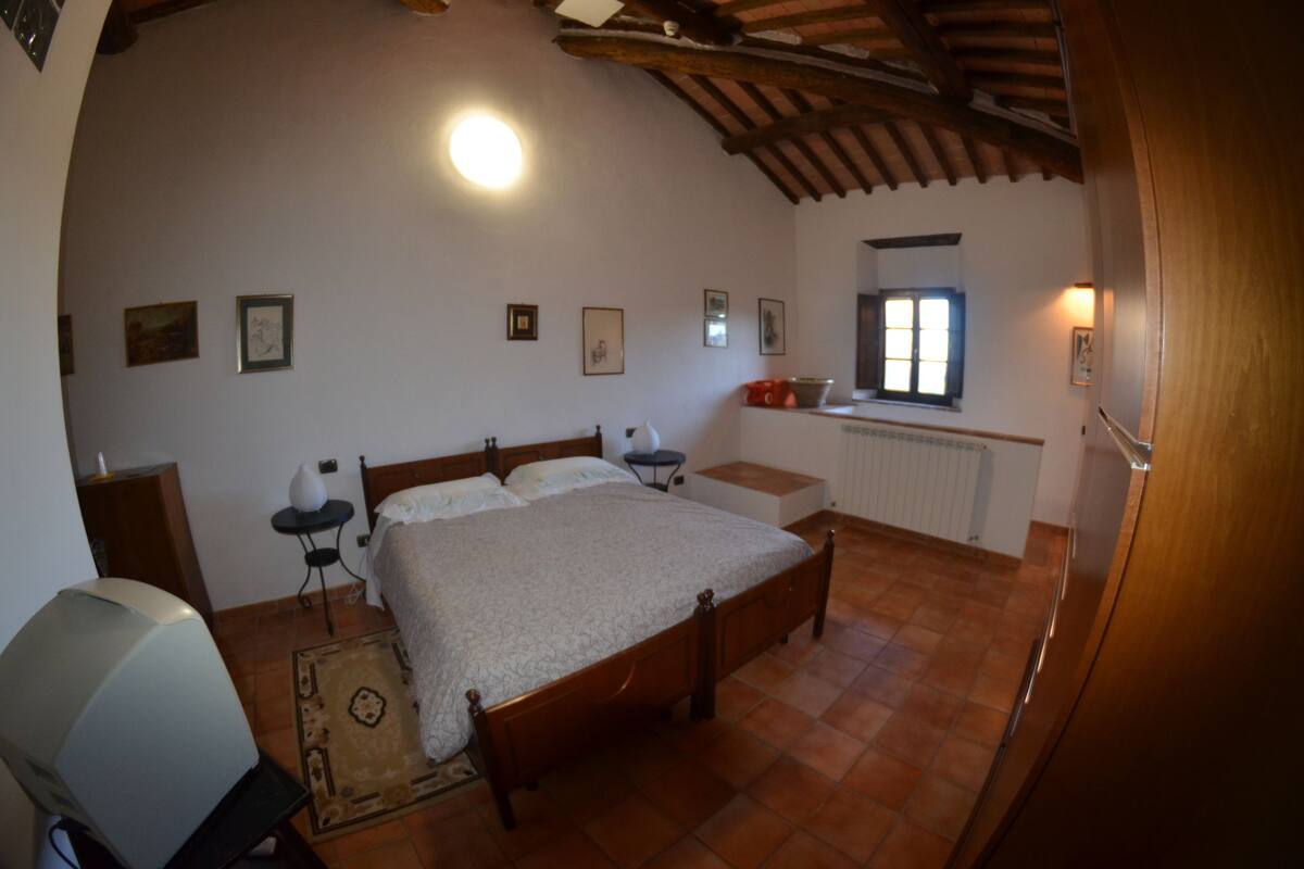 A bedroom with a large bed, a bedside table, a chair, a radiator, and a window with curtains.
