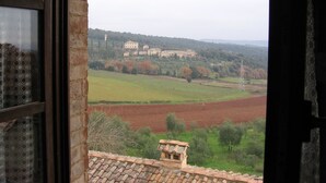 Panorama di una campagna con un grande edificio in lontananza, campi coltivati e una torre di linee elettriche.