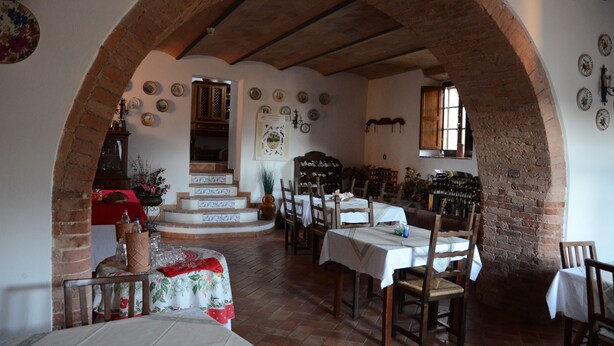 Zona pranzo con archi in mattoni, tavoli e sedie in legno. Si vedono piatti e una credenza per vini alle pareti.