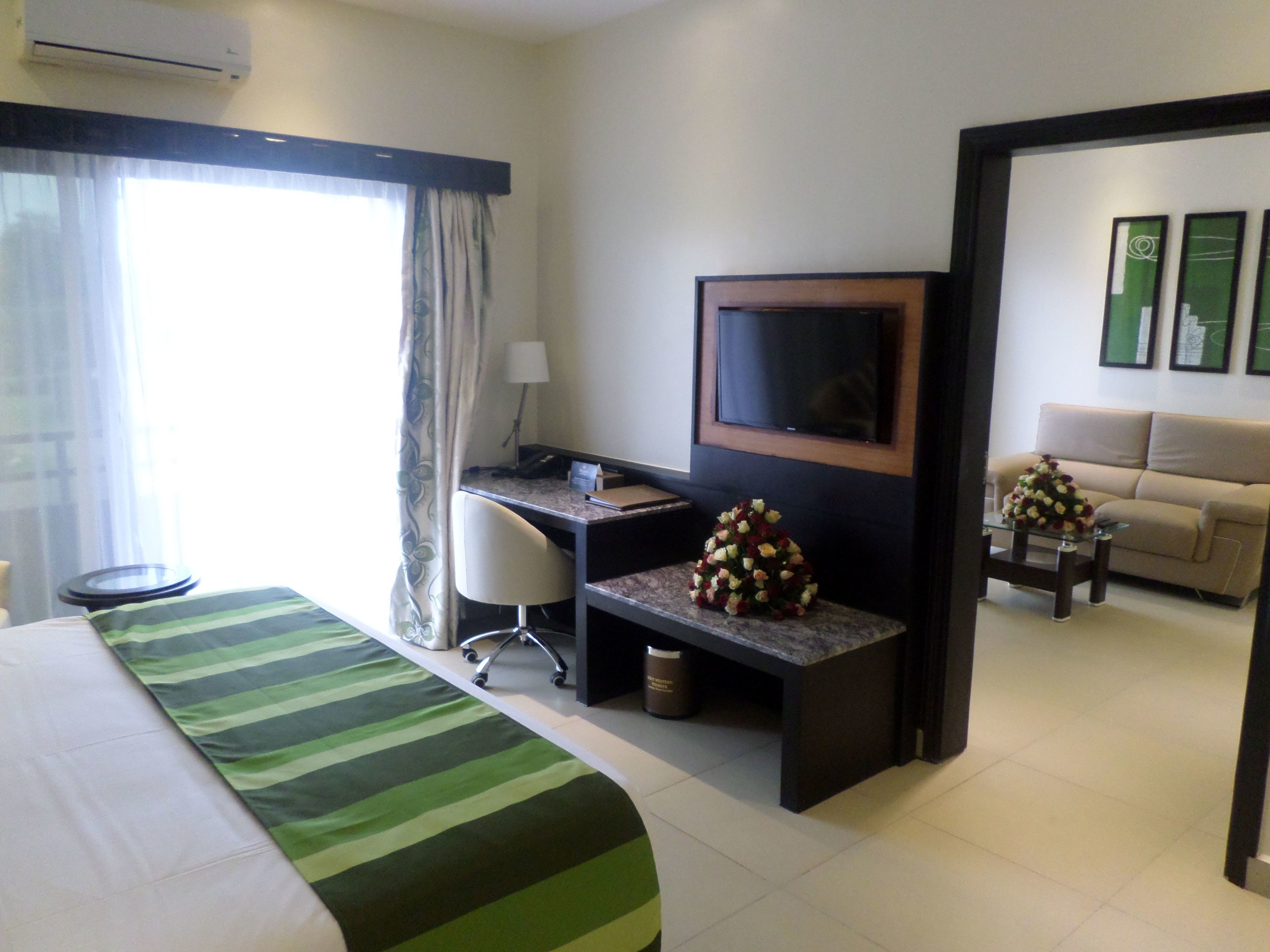 A hotel room with a bed, a desk, a TV, a sofa, and a window with curtains.