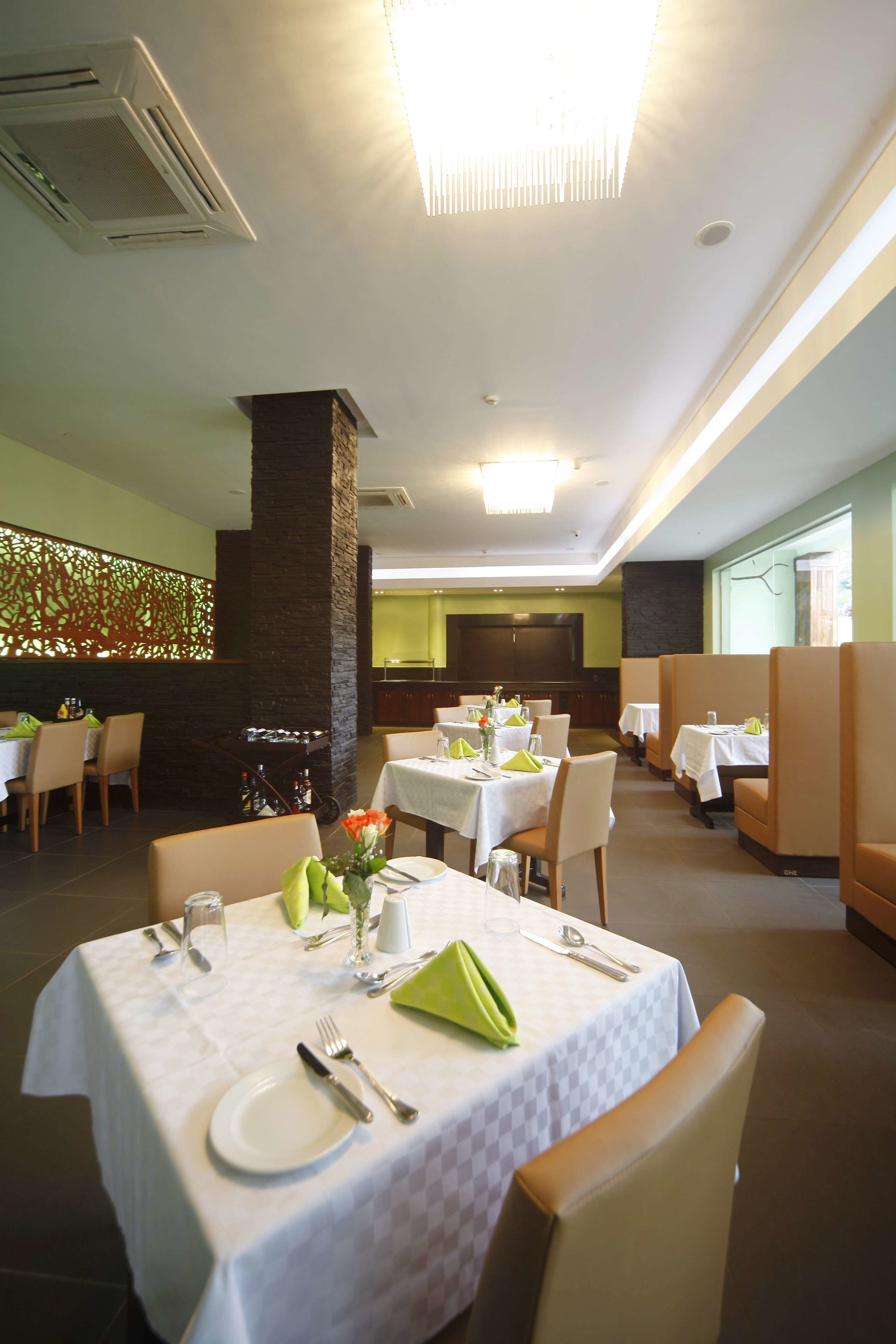 A restaurant with tables set for dining, a stone pillar, and a television screen in the background.
