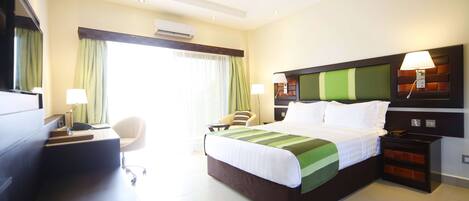 Una habitación de hotel con cama, escritorio, silla, mesitas de noche y una ventana con cortinas.