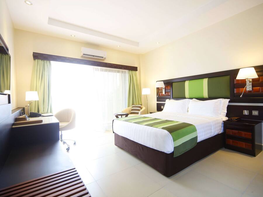 A hotel room with a bed, desk, chair, bedside tables, and a window with curtains.