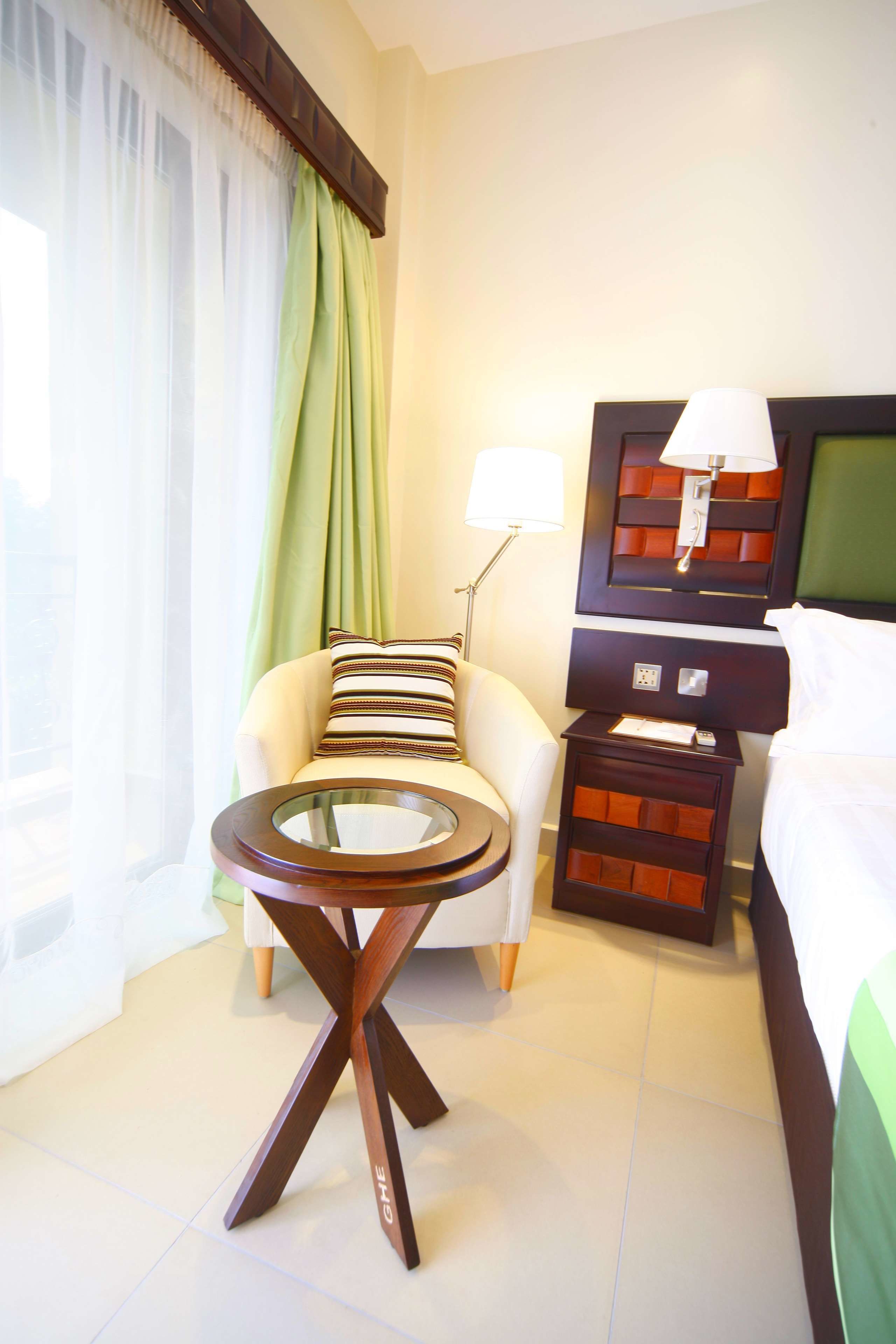 A hotel room with a bed, a chair, a small table, and a nightstand.