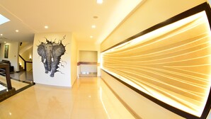 A modern hallway with a unique wall art of an elephant breaking through a wall, a staircase, and a wall with illuminated lines. - Best Western Premier Garden Hotel Entebbe (Entebbe)