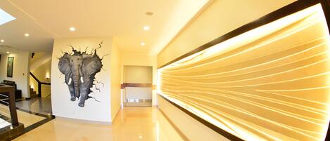 A modern hallway with a unique wall art of an elephant breaking through a wall, a staircase, and a wall with illuminated lines.