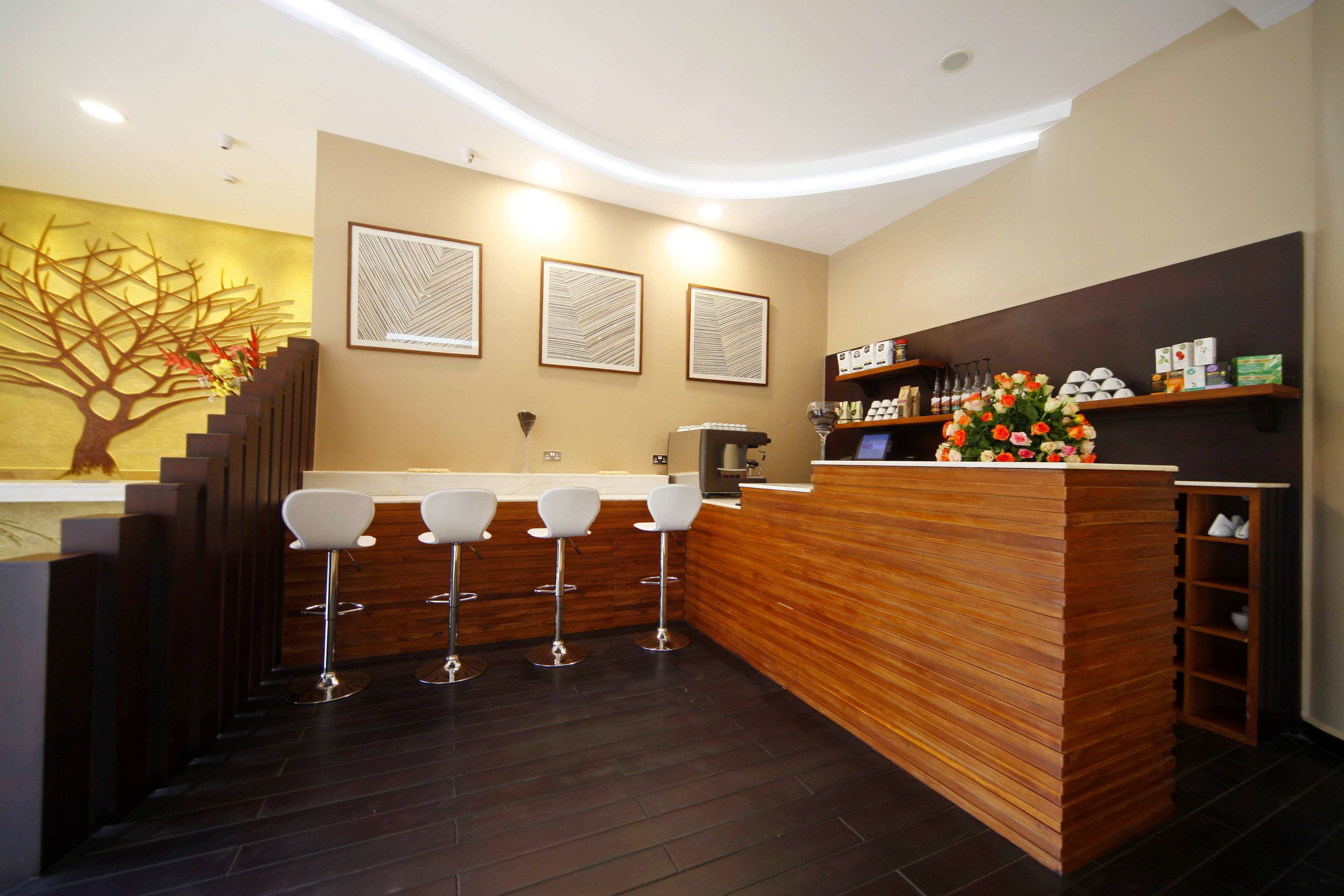 A modern bar area with a wooden counter, four white bar stools, and a decorative tree mural on the wall.