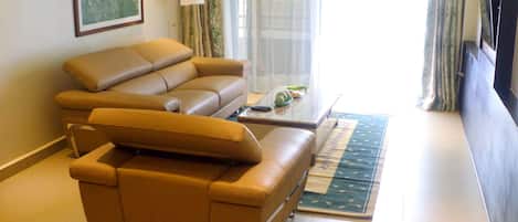 Una sala de estar con un sofá de cuero marrón, una mesa de centro y un televisor sobre un mueble.