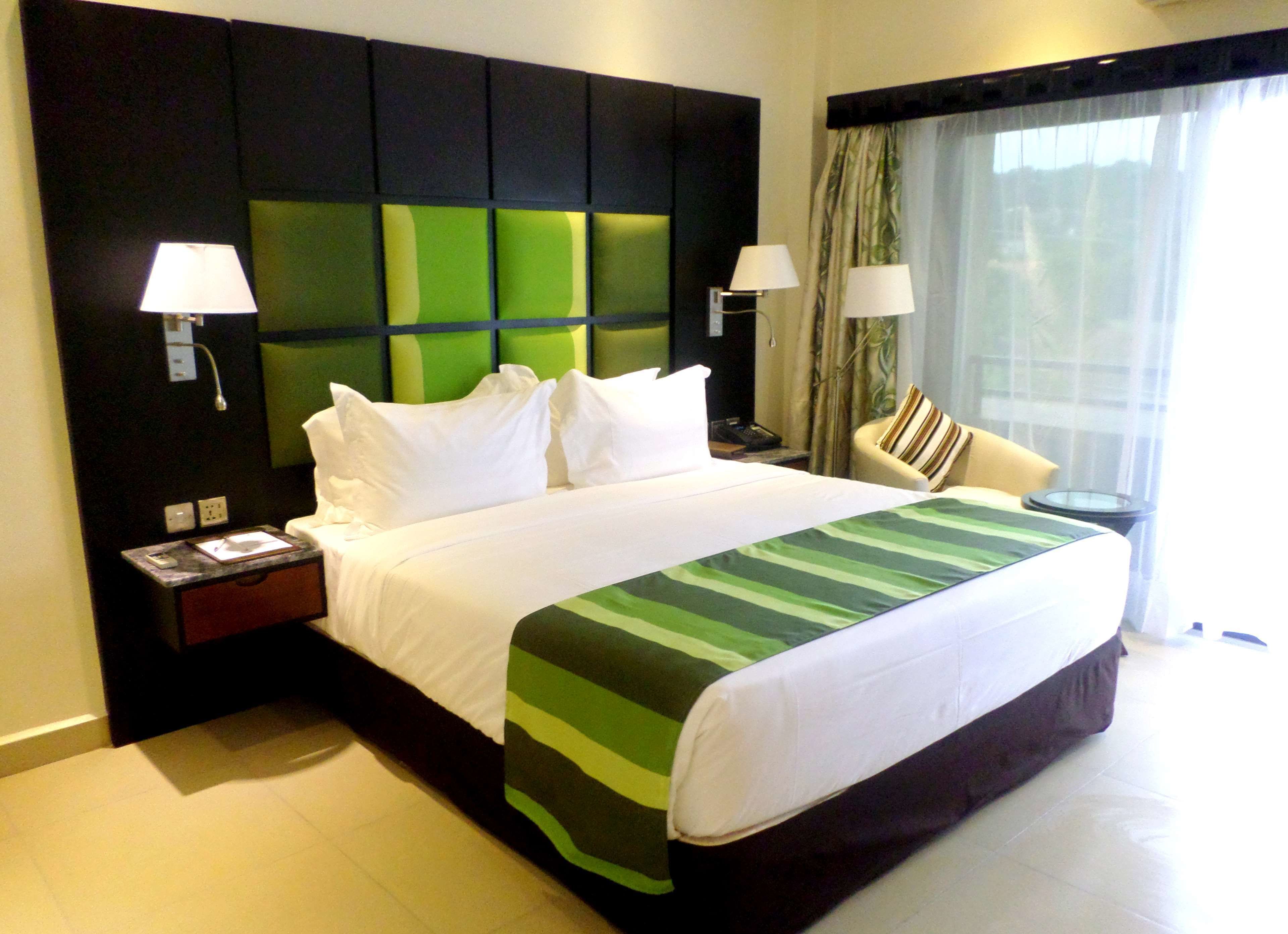 A hotel room with a large bed, two bedside tables, a nightstand, a chair, and a window with curtains.