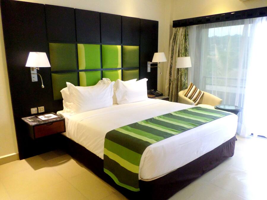 Una habitación de hotel con una cama grande, dos mesitas de noche, una silla y una ventana con cortinas.