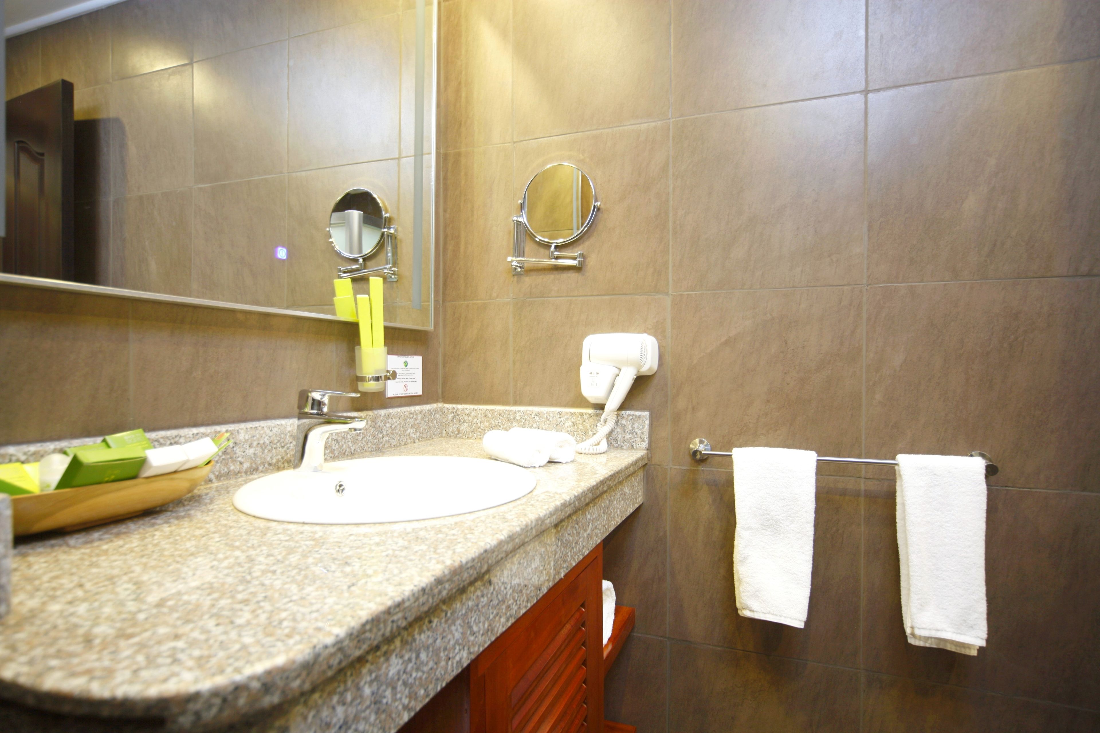 Une salle de bain dotée d’un comptoir en granit, d’un lavabo, d’un miroir, d’un porte-serviettes et d’un sèche-mains.
