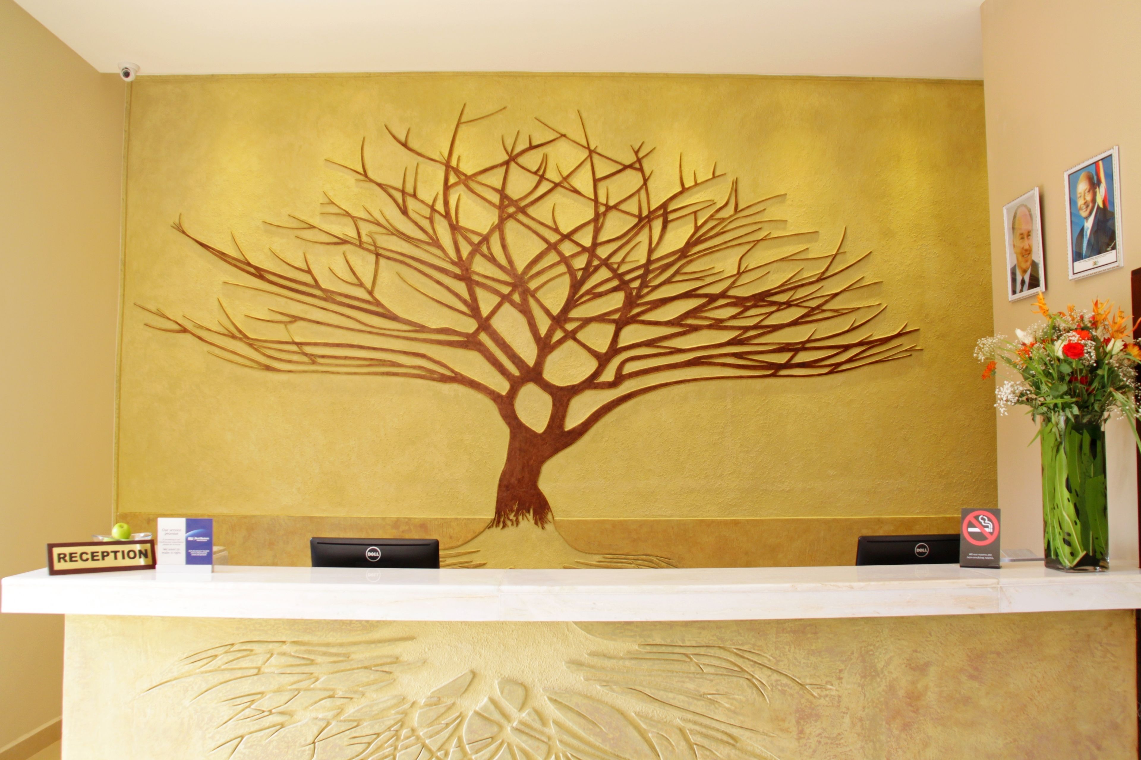 A reception desk with a large tree mural, a 'Reception' sign, a no-smoking sign, and a vase with flowers.