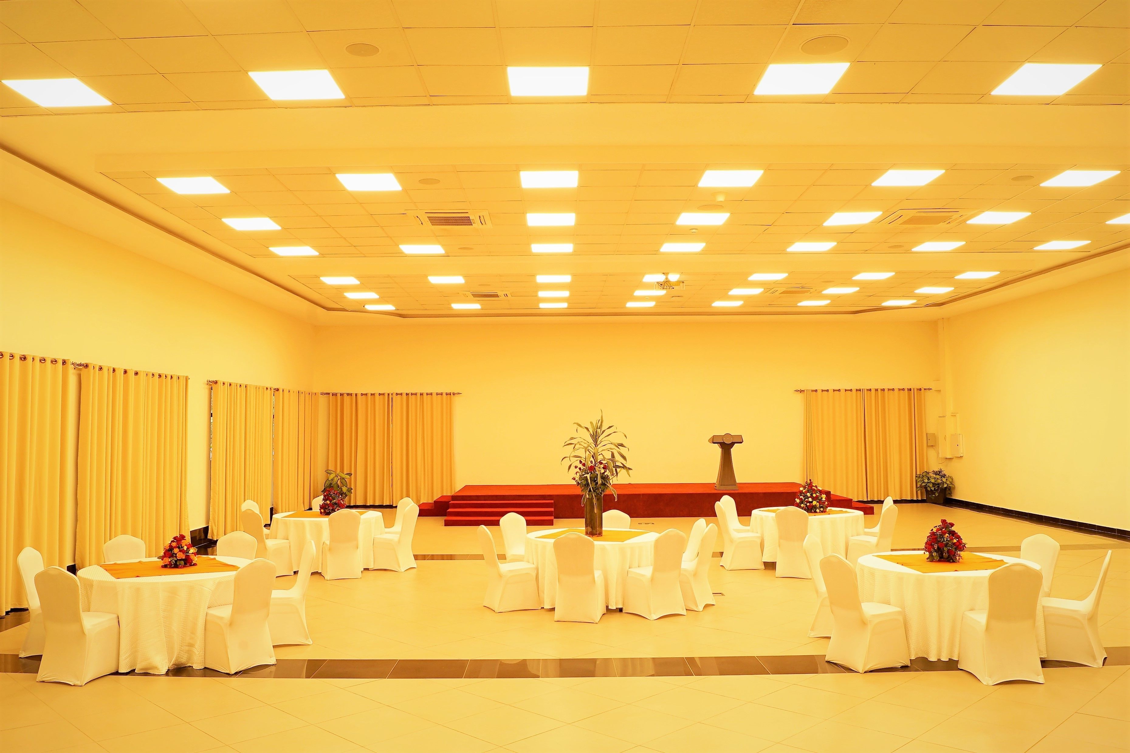 A conference room with multiple round tables, white chairs, and a stage with a podium.