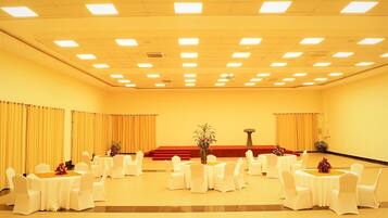 Un salón de conferencias con varias mesas redondas, sillas blancas y un escenario con un atril.