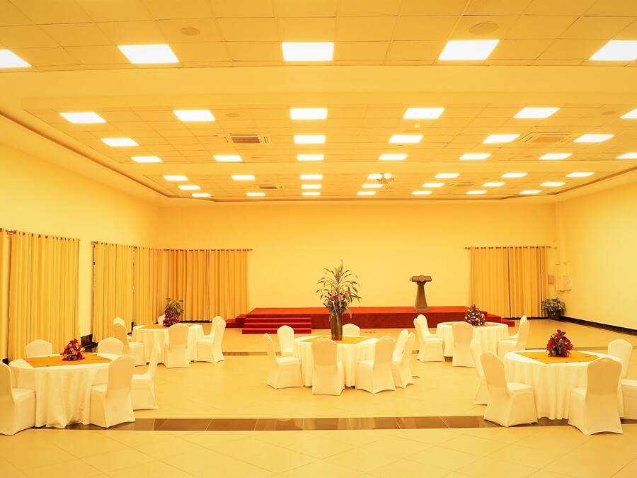 Un salón de conferencias con varias mesas redondas, sillas blancas y un escenario con un atril.