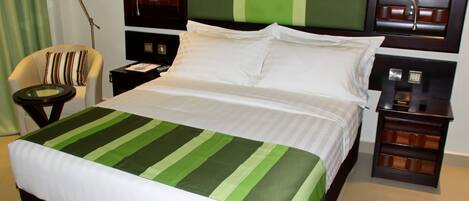 A hotel room with a bed, a chair, a nightstand, and a lamp.