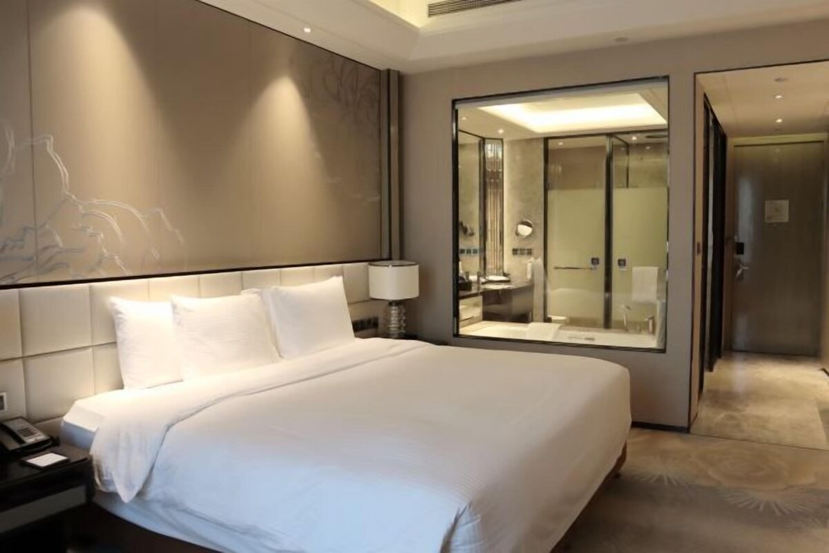 A hotel room with a large bed, a nightstand, a mirror, and a sliding door leading to a bathroom.