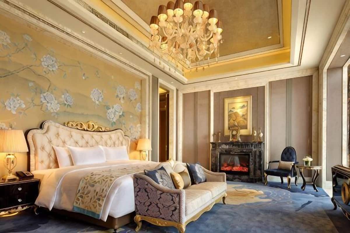 A luxurious bedroom with a large bed, a sofa, a fireplace, and a chandelier.