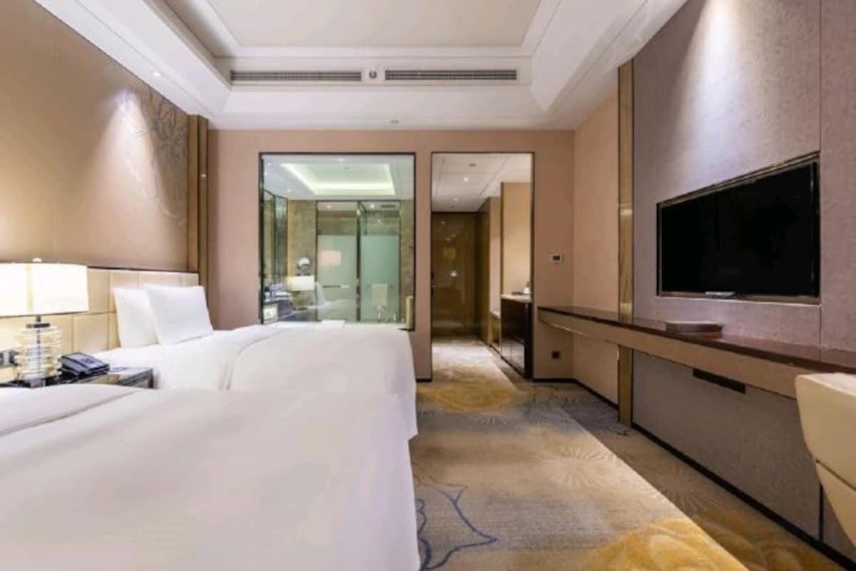 A hotel room with a bed, bedside table, lamp, TV, and a mirror.