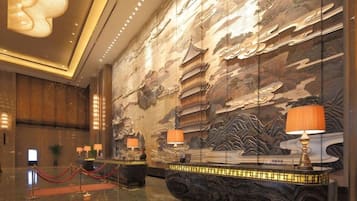 Eine Lobby mit einer Rezeption, roten Absperrseilen und einem großen Wandbild mit traditioneller asiatischer Kunst.