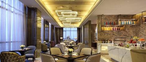A hotel dining area with a long table, chairs, and a bar with bottles.