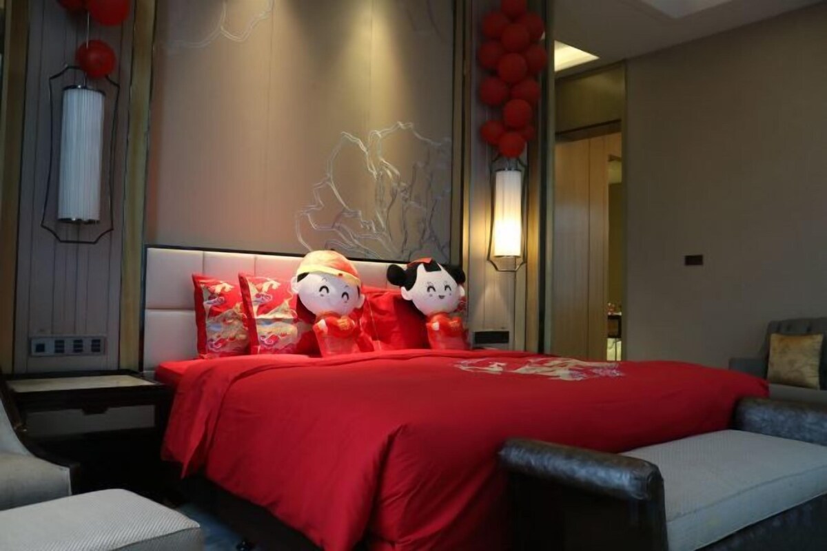 A hotel room with a large bed, two decorative pillows, a nightstand, and a wall-mounted lamp.
