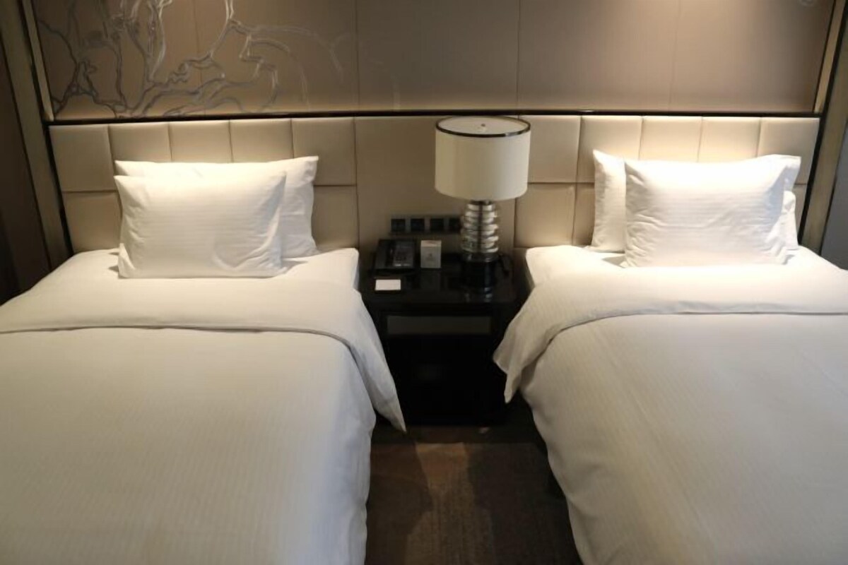 A hotel room with two beds, a nightstand with a lamp, and a wall with a decorative panel.