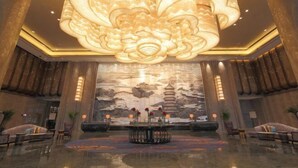 A spacious lobby with a large, ornate chandelier, a central round table with flowers, and traditional Asian architectural elements on the walls. - Wanda Realm Fuyang (Fuyang)