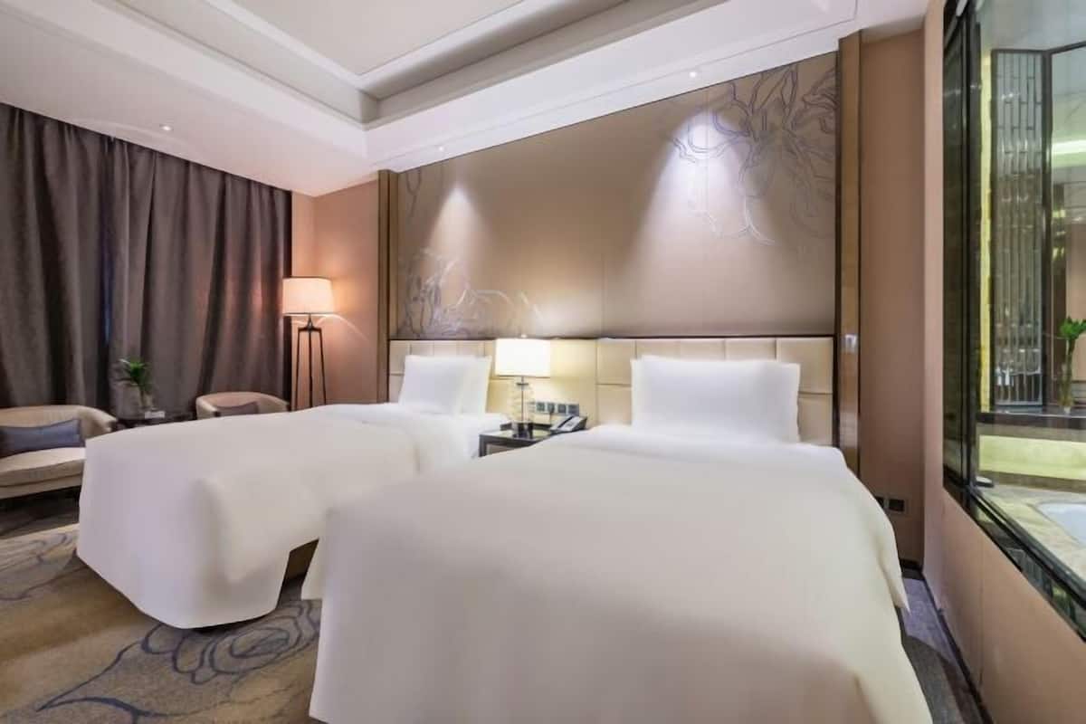 A hotel room with two beds, a sofa, a lamp, and a view of the outside.