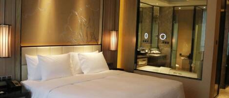 A hotel room with a large bed, bedside lamps, a mirror, and a view of the bathroom.