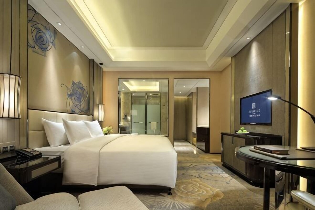 A hotel room with a large bed, bedside tables, a desk, and a television.