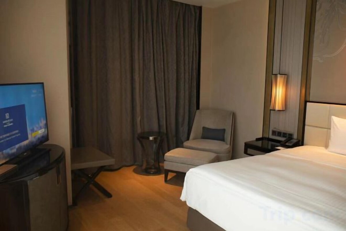 A hotel room with a bed, a desk with a computer, a chair, a small table, a lamp, and a curtain.