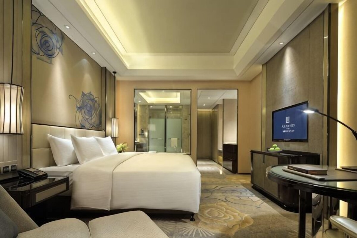 A hotel room with a bed, bedside tables, a TV, a desk, and a mirror.