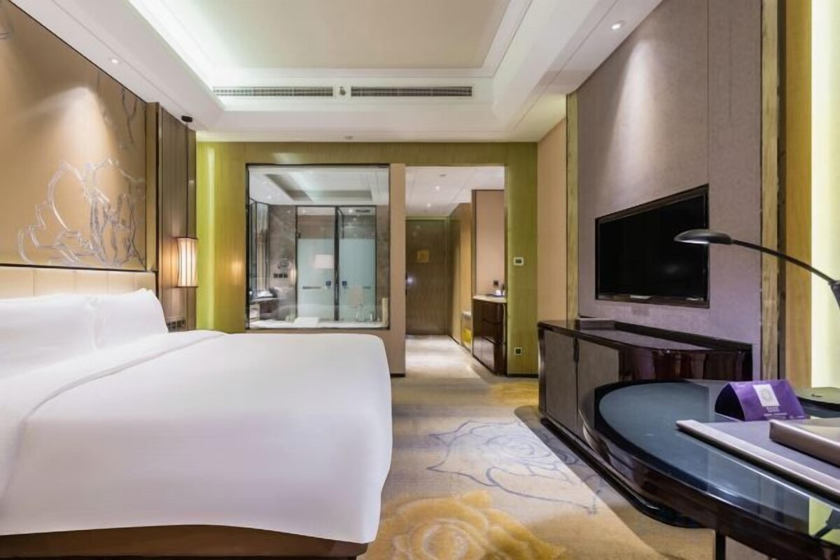 A hotel room with a large bed, a flat-screen TV, a desk, and a bathroom visible through an open door.