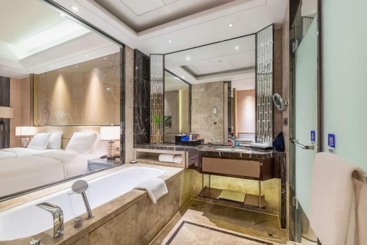 A modern bathroom with a large mirror, a bathtub, a vanity with a sink, and a toilet.