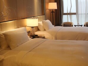 A hotel room with two beds, a nightstand with a lamp, and a view of the outdoors through the window.